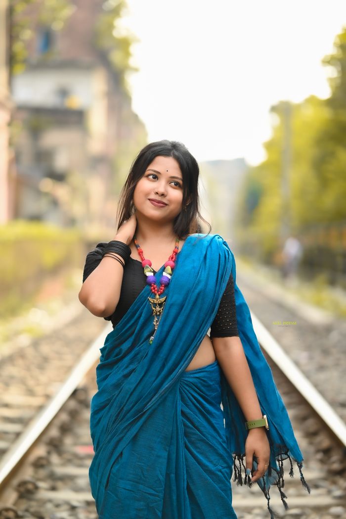 A beautiful woman in a blue saree poses on railway tracks in Kolkata, India.