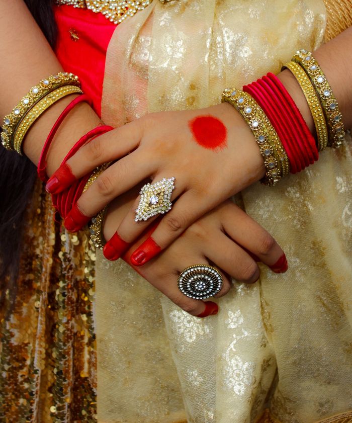 Close-up of hands adorned with traditional red and gold jewelry, showcasing cultural beauty.